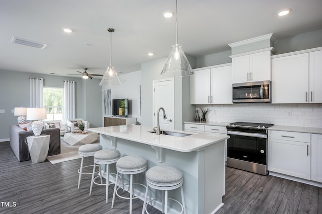 kitchen featuring stainless steel appliances, a kitchen island with sink, sink, pendant lighting, and white cabinets