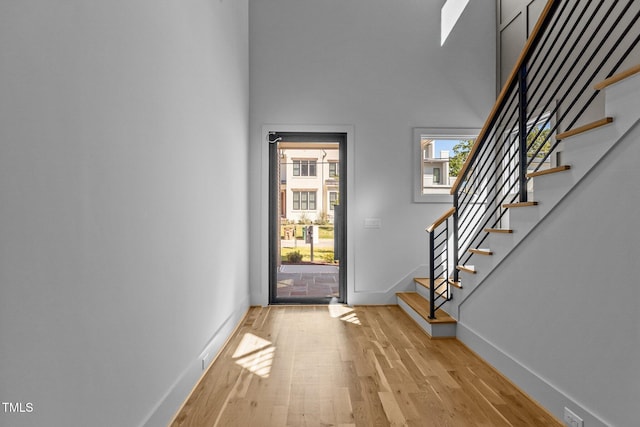 foyer featuring baseboards, light wood-style flooring, stairway, and a towering ceiling