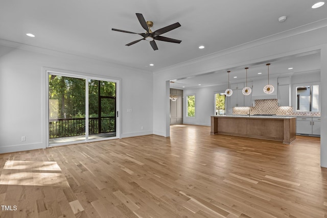 unfurnished living room with recessed lighting, light wood finished floors, crown molding, plenty of natural light, and baseboards