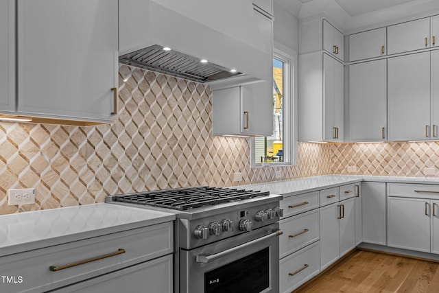 kitchen with high end stainless steel range, custom exhaust hood, light countertops, and backsplash