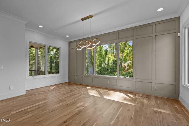 unfurnished dining area with a decorative wall, crown molding, a chandelier, light wood-type flooring, and baseboards