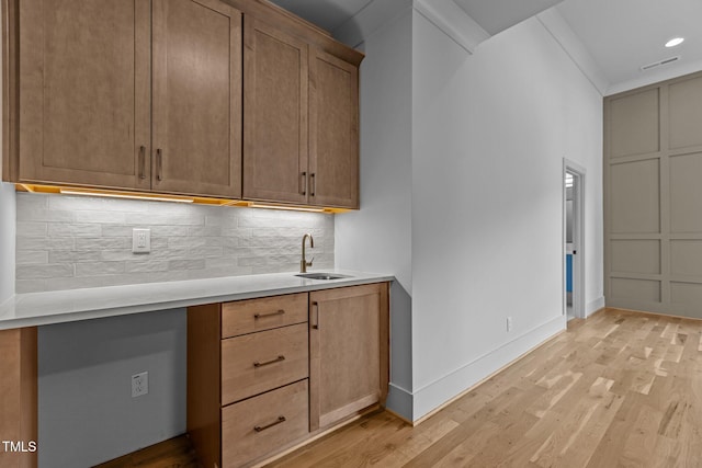 kitchen featuring a sink, light wood-style flooring, tasteful backsplash, light countertops, and baseboards
