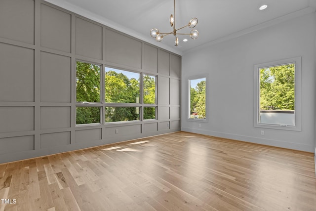 unfurnished room with a decorative wall, a chandelier, crown molding, and light wood-style flooring