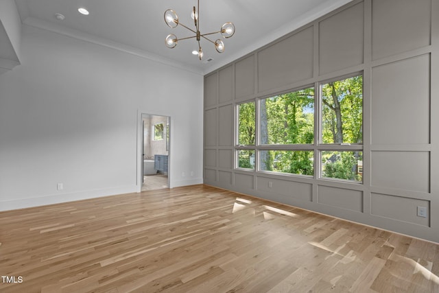 unfurnished dining area featuring a decorative wall, a chandelier, light wood finished floors, a high ceiling, and crown molding