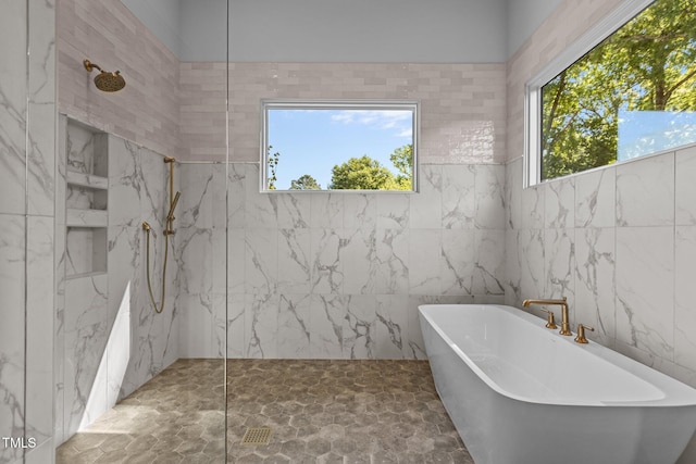 full bathroom with a freestanding tub, a marble finish shower, and tile walls