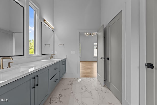 bathroom featuring marble look tiles, double vanity, a chandelier, and baseboards