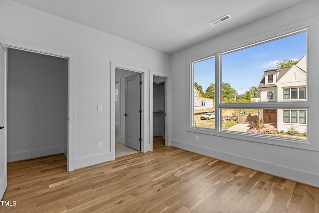 unfurnished bedroom featuring a walk in closet, baseboards, light wood-style floors, and a closet