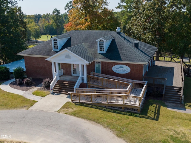 view of front facade with a wooden deck, a shingled roof, a front lawn, concrete driveway, and brick siding