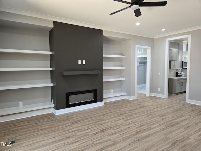 unfurnished living room with built in shelves, baseboards, ornamental molding, a glass covered fireplace, and light wood-type flooring