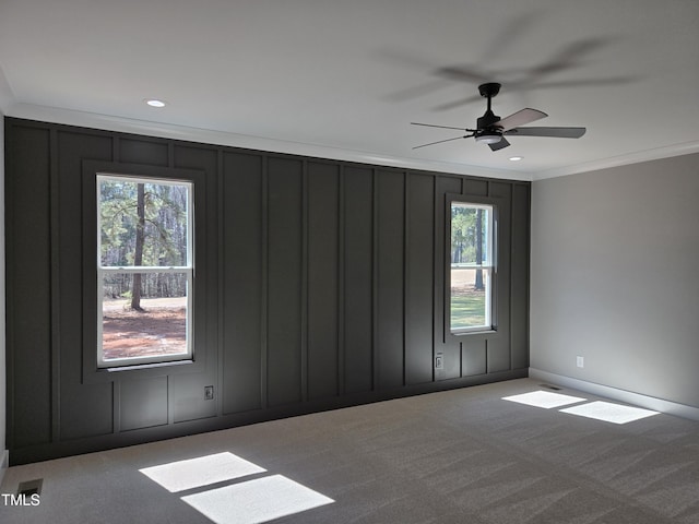 carpeted empty room featuring a wealth of natural light, ornamental molding, and a decorative wall