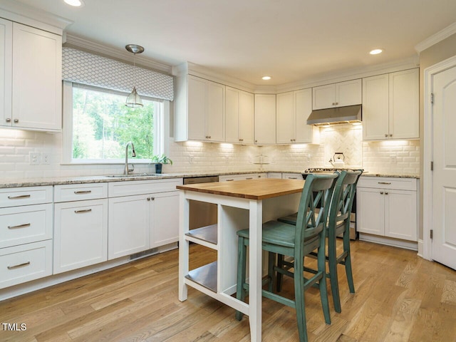 kitchen with white cabinetry, hanging light fixtures, butcher block countertops, sink, and light hardwood / wood-style flooring