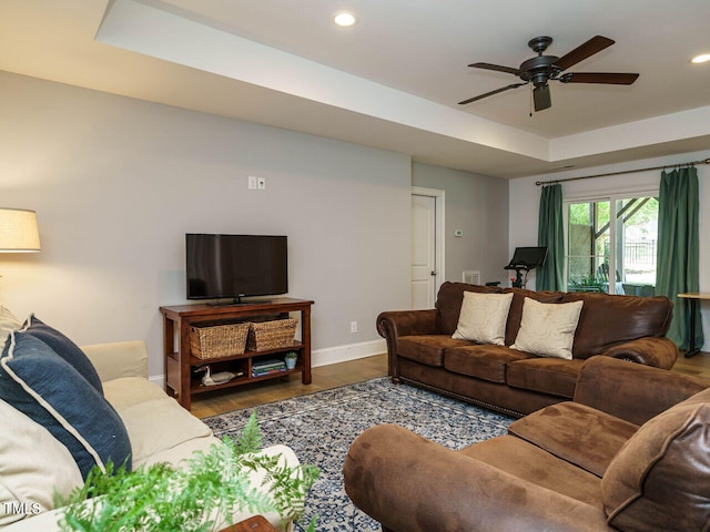 living room with a raised ceiling, ceiling fan, and dark hardwood / wood-style flooring