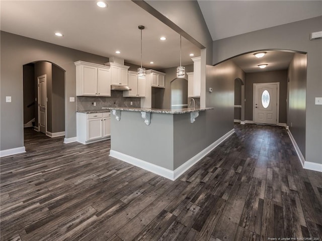 kitchen featuring white cabinetry, vaulted ceiling, light stone counters, decorative backsplash, and pendant lighting