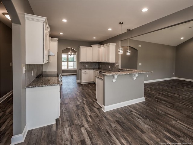 kitchen featuring white cabinets, dark stone countertops, kitchen peninsula, decorative backsplash, and hanging light fixtures