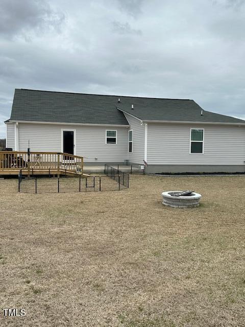 rear view of property featuring a deck, a fire pit, and a lawn