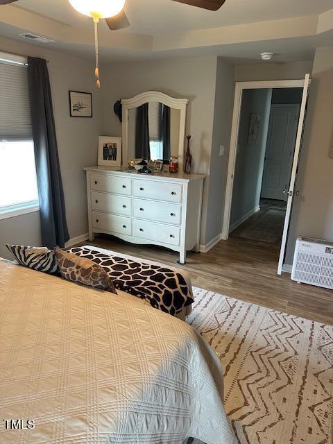 bedroom with wood-type flooring, a wall mounted AC, and ceiling fan