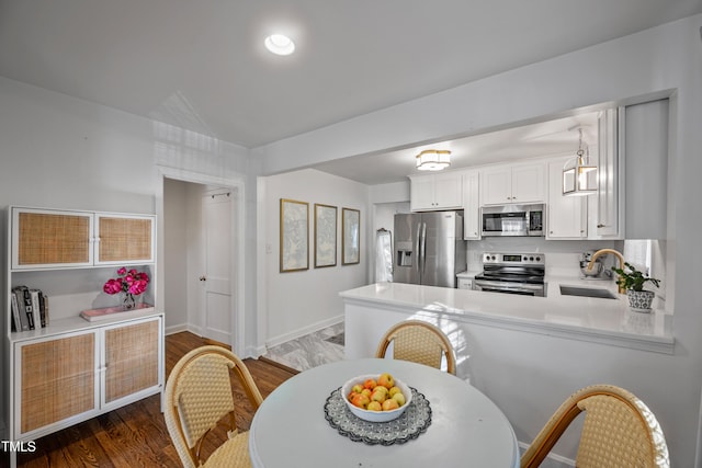 kitchen featuring white cabinets, stainless steel appliances, kitchen peninsula, dark wood-type flooring, and sink