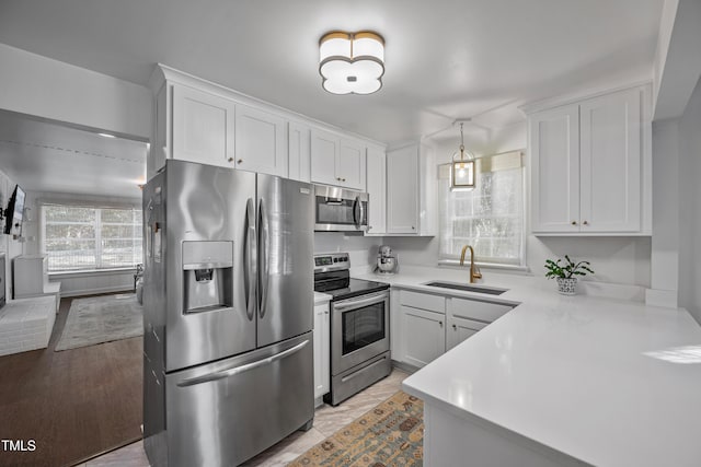 kitchen featuring stainless steel appliances, sink, white cabinetry, kitchen peninsula, and hanging light fixtures