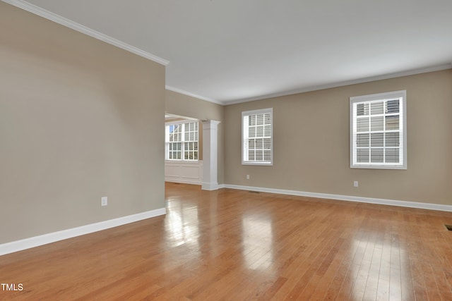 spare room featuring crown molding, decorative columns, and light wood-type flooring