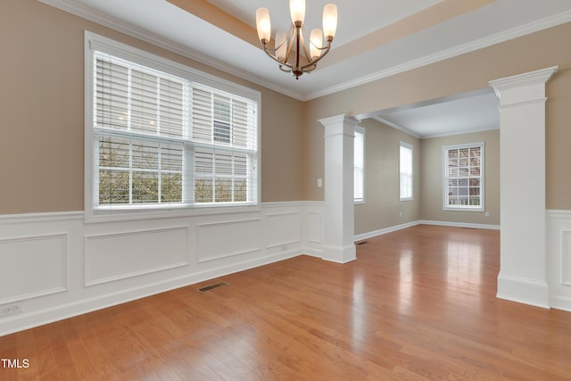 unfurnished room with a notable chandelier, ornamental molding, light wood-type flooring, and ornate columns