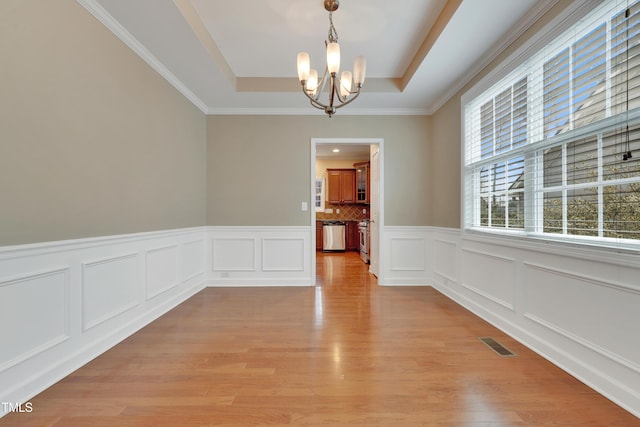 empty room featuring a raised ceiling, crown molding, a notable chandelier, and light hardwood / wood-style flooring