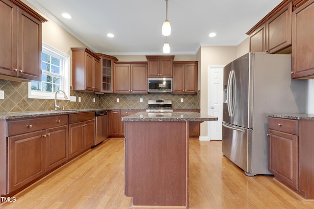 kitchen with pendant lighting, stainless steel appliances, a kitchen island, and light hardwood / wood-style flooring