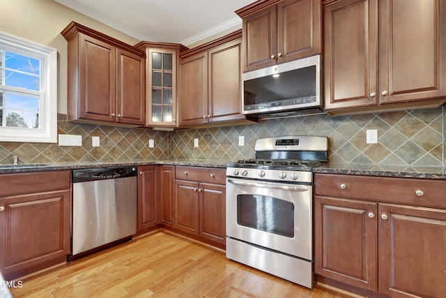 kitchen featuring appliances with stainless steel finishes, dark stone countertops, ornamental molding, light hardwood / wood-style floors, and decorative backsplash