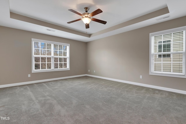 carpeted spare room with a raised ceiling and ceiling fan