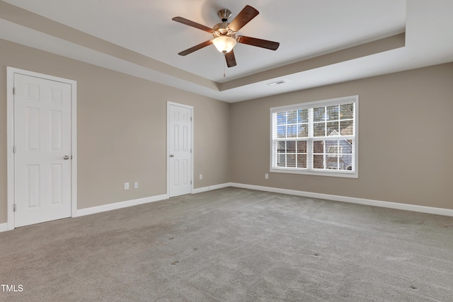 unfurnished room with ceiling fan, a tray ceiling, and light carpet