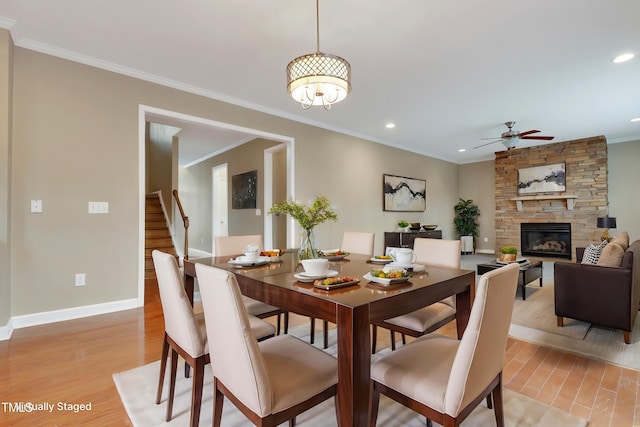 dining area with a stone fireplace, light hardwood / wood-style flooring, ornamental molding, and ceiling fan