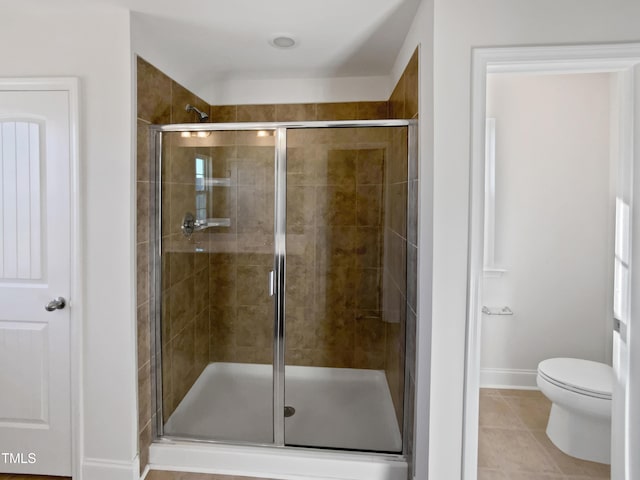 bathroom featuring tile patterned flooring, a shower with door, and toilet