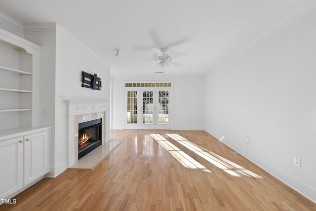 unfurnished living room with french doors, built in features, ornamental molding, light wood-type flooring, and ceiling fan