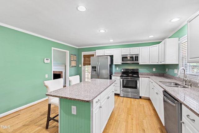 kitchen with sink, stainless steel appliances, a kitchen breakfast bar, white cabinets, and a kitchen island