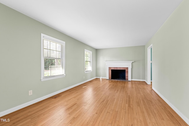 unfurnished living room featuring a brick fireplace and light hardwood / wood-style flooring