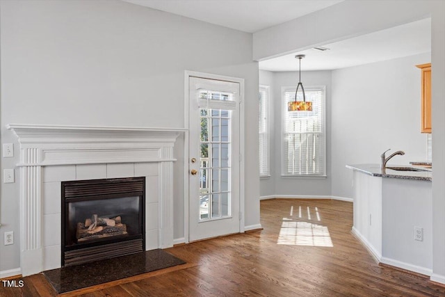 unfurnished living room featuring sink, a tiled fireplace, and hardwood / wood-style flooring