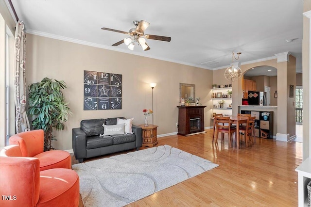 living room featuring ceiling fan with notable chandelier, a fireplace, hardwood / wood-style floors, and crown molding