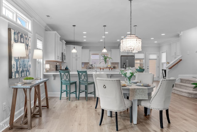 dining space with sink, light hardwood / wood-style flooring, crown molding, and a notable chandelier