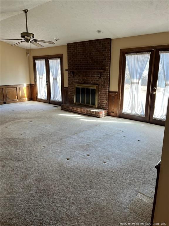 unfurnished living room with ceiling fan, a healthy amount of sunlight, french doors, and a fireplace