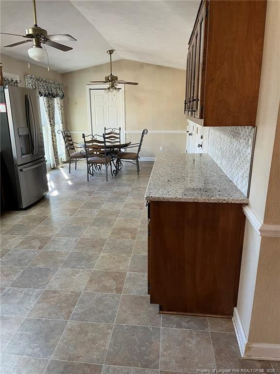 kitchen with ceiling fan, lofted ceiling, light stone counters, and stainless steel refrigerator with ice dispenser