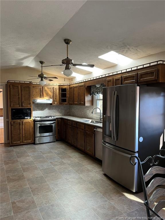 kitchen featuring sink, a textured ceiling, vaulted ceiling, tasteful backsplash, and appliances with stainless steel finishes