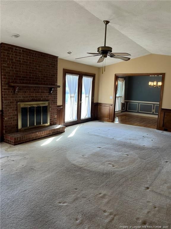 unfurnished living room with a textured ceiling, a fireplace, vaulted ceiling, french doors, and ceiling fan