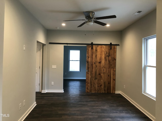 spare room with a barn door, ceiling fan, and dark hardwood / wood-style floors