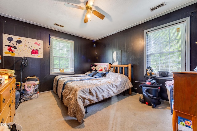 bedroom with light carpet, a textured ceiling, ceiling fan, and wood walls