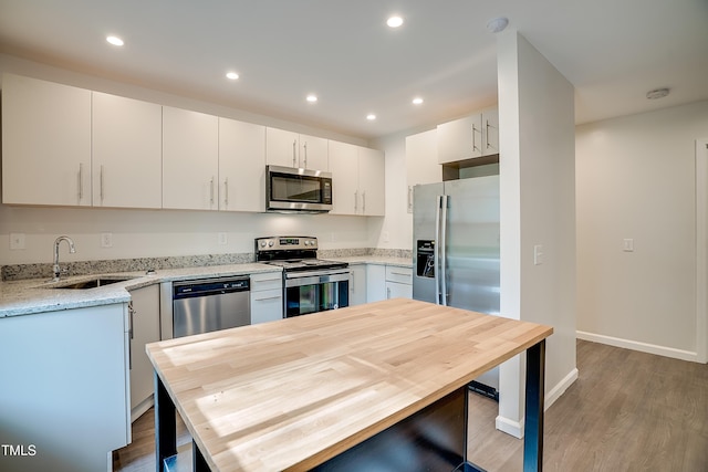 kitchen with appliances with stainless steel finishes, light stone counters, sink, white cabinets, and hardwood / wood-style floors