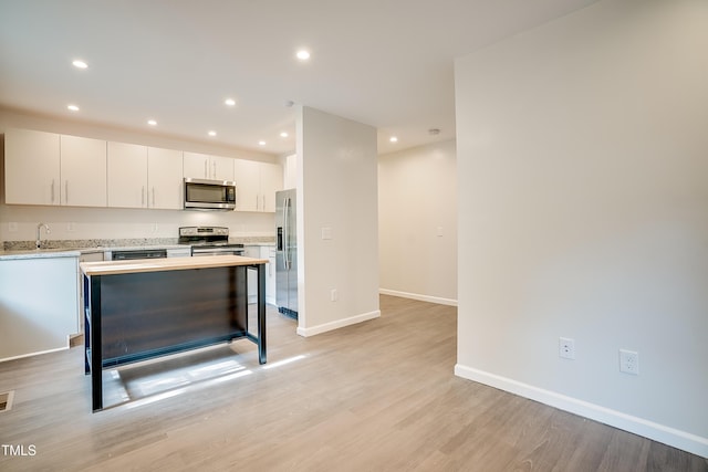 kitchen featuring sink, light hardwood / wood-style flooring, a kitchen island, white cabinetry, and stainless steel appliances