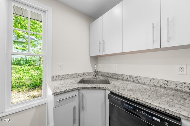 kitchen featuring black dishwasher, a sink, white cabinetry, and light stone counters