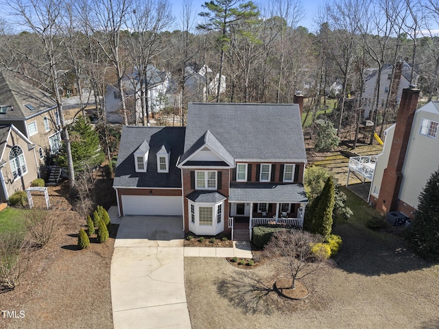 traditional-style house featuring a garage, driveway, a residential view, a porch, and brick siding