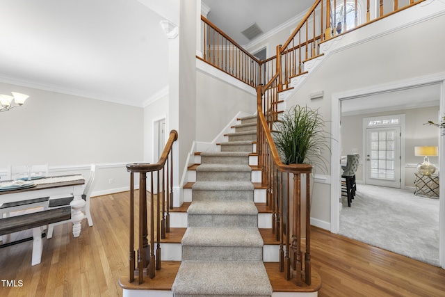 staircase featuring a towering ceiling, ornamental molding, wood finished floors, a chandelier, and baseboards