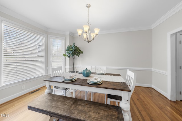 dining room with ornamental molding, wood finished floors, visible vents, and an inviting chandelier