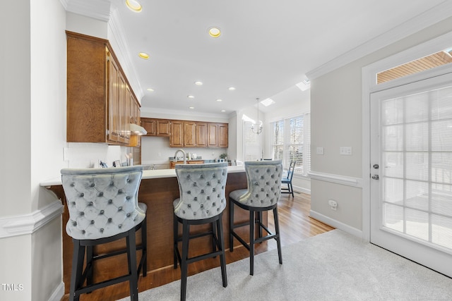 kitchen featuring a peninsula, light countertops, brown cabinetry, decorative light fixtures, and crown molding